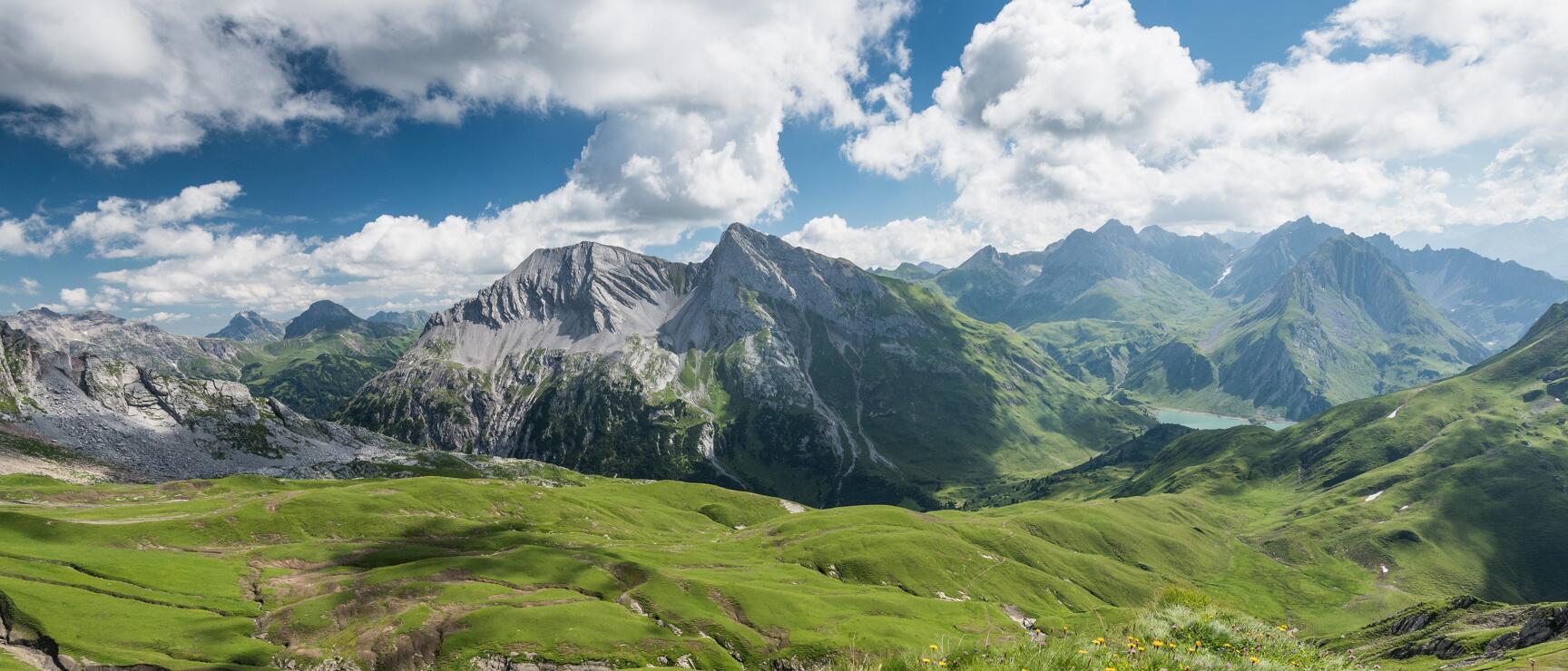 Alpine panorama with peaks, meadows and a turquoise lake