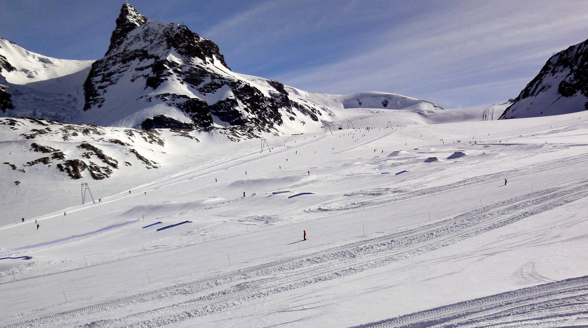 Ski slope with skiers, chairlifts and snowy peaks
